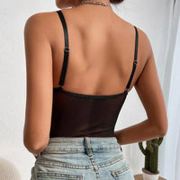 Person wearing a black strappy top and blue jeans against a white wall.